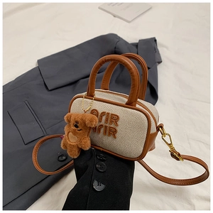 Detail of canvas bowling bag with brown leather handles and a plush teddy bear charm
