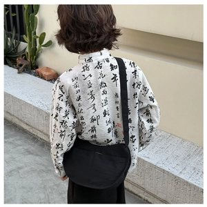 Close-up of minimalist black moon-shaped crossbody bag on a child's artistic street outfit
