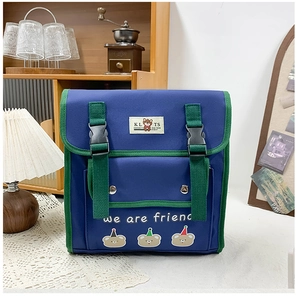 Detail of color-block canvas backpack featuring cartoon bear embroidery and buckle straps