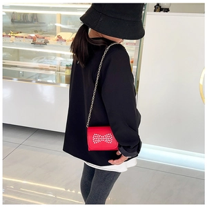 Detail of red girls shoulder bag featuring pearl bow decoration and golden chain strap