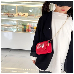 Detail view of red girls' shoulder bag with pearl bow and golden chain strap on a model