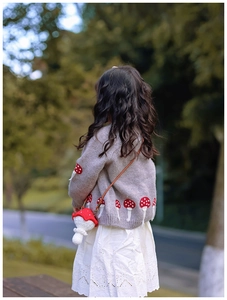 Détail d'un petit sac champignon crocheté main avec un cardigan en maille grise