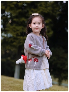 Détail d'un sac champignon en crochet rouge et blanc avec cardigan gris pour enfants