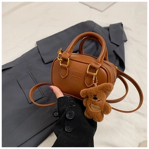 Detailaufnahme der karamellbraunen Mini-Tasche mit Bärenanhänger und Prägung