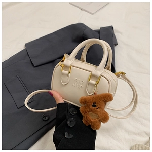 Nahaufnahme der beigen Mini-Boston-Tasche aus Leder mit Bärenanhänger auf grauem Anzug