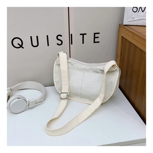 Detail of a creamy white nylon crescent bag with dual front pockets and wide strap