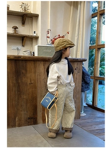 Kid wearing stylish beige sweater and quilted pants with a mini blue crossbody bag