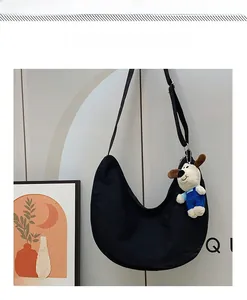 Close-up of black canvas crescent bag with cute puppy plush charm and wide strap