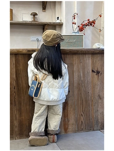 Detail of a quilted beige kids' winter jacket and a blue crossbody bag with embroidery