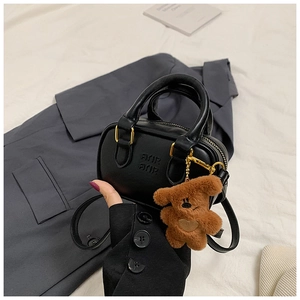Detail einer schwarzen Handtasche mit Plüschbären-Anhänger und geprägter Aufschrift