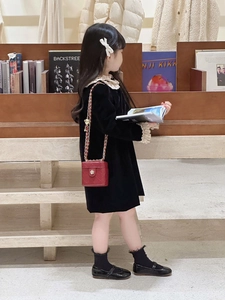 Girl wearing black velvet dress and red quilted mini bag in a cozy library setting