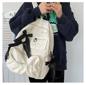 Dettaglio dello zaino in nylon bianco con fiocchi in nastro nero e pratiche tasche con cerniera