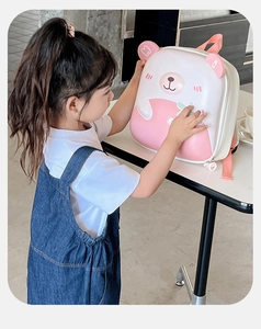 Pink and white hardshell bear backpack for kids shown with a child in a cozy scene