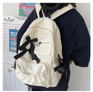 Vista dettagliata di uno zaino scolastico crema con fiocchi neri e tasca con zip sul retro