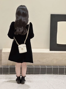 Detail of a white quilted crossbody mini bag with gold chain strap on a black velvet dress