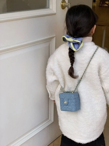 Close-up of blue tweed mini vanity bag with gold chain strap on a child model