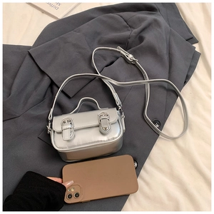 Detail view of mini silver metallic bag with dual buckles and slim strap on grey fabric