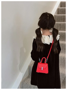 Red mini leather crossbody bag for kids shown on model in a stylish indoor setting