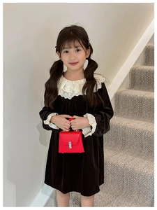 Close-up of a black velvet kid's dress with white lace collar and red handbag accessory
