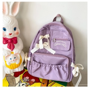 Dettaglio dello zaino in nylon viola con fiocchi bianchi e tasca anteriore plissettata
