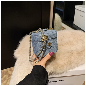 Detail of blue denim quilted mini box bag with gold chain and camellia flower clasp