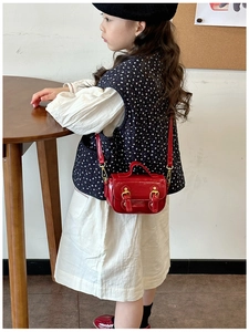 Detail view of a glossy red oil wax leather mini crossbody bag with gold buckles for girls