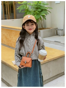Close-up of a mini brown leather crossbody bag styled with a grey knit sweater and denim skirt