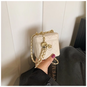 Detail of cream quilted mini bag featuring gold flower clasp and woven chain strap
