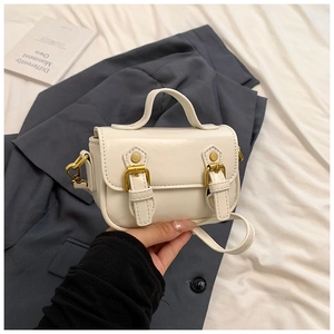 Detail of a beige faux leather mini satchel with golden buckles and top handle strap