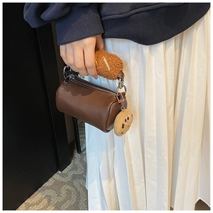 Détail d'un sac cylindrique marron avec poignée en peluche et pendentif biscuit