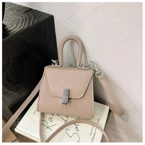 Detail of beige mini crossbody bag with litchi texture on a white book prop