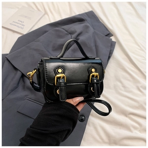 Detail of black oil wax leather mini handbag with gold buckles and rivets in a lifestyle setting