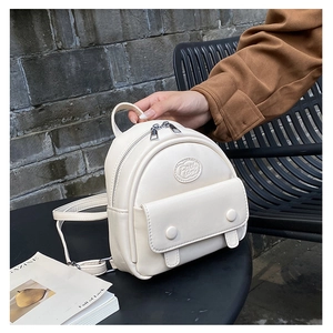 Detail of a creamy white mini leather backpack featuring lychee texture and front flap pocket