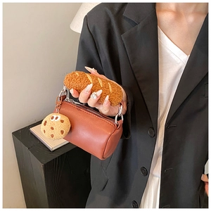 Détail d'un sac à main cylindrique marron avec une anse baguette en peluche et un charme biscuit
