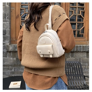 Detail of cream white mini PU leather backpack featuring circular logo and front flap pocket
