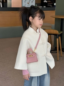 Mini sac bandoulière rose pour fille porté avec un manteau blanc dans un café