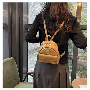 Mini khaki leather backpack shown on model in a cozy cafe setting for daily commute