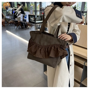 Detail of a brown canvas tote bag featuring stylish ruffle pleats and wide shoulder straps