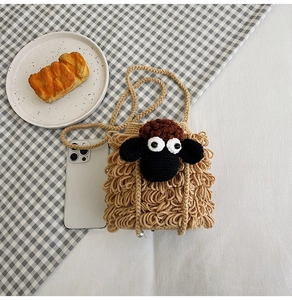 Detail of hand-knitted cartoon sheep crossbody bag with woven strap and decorative pearl