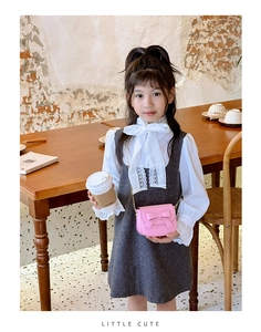Close-up of pink girls' bow crossbody bag with gold chain strap on a wooden table