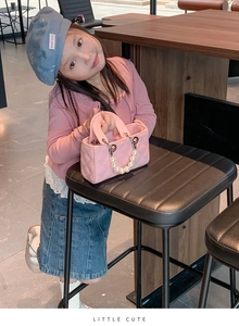 Detailed view of pink quilted kids handbag featuring a pearl handle on a young model
