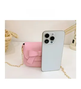 Pink mini crossbody bag size comparison with a smartphone on a white desk backdrop