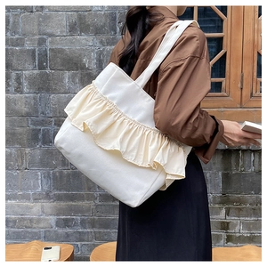 Close-up of cream canvas tote bag featuring decorative ruffles and thick shoulder strap