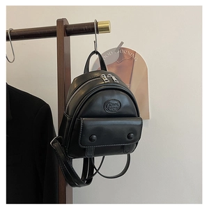 Detail of a minimalist black mini backpack in PU leather hanging on a wooden rack