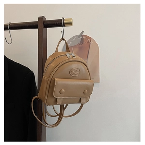 Detail view of khaki mini backpack hanging on wooden rack featuring front flap pocket