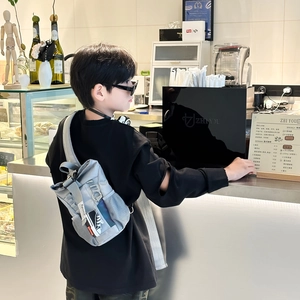 Child wearing modern grey crossbody chest bag with sporty sneaker pendant in a cafe setting