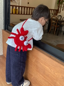 Detail of red crochet crab shoulder bag with hand-knitted texture on a child model
