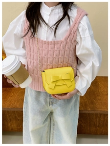 Girl's bright yellow crossbody bag with large bow detail and gold chain strap on model
