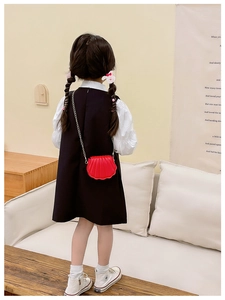 Détail du sac rouge en forme de coquillage avec chaîne dorée porté par une petite fille