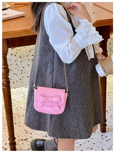 Detailed view of pink mini shoulder bag with bow and gold chain on young model